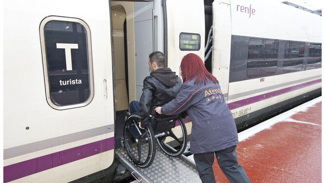 Una persona con movilidad reducida es ayudada para acceder a un tren de Renfe.