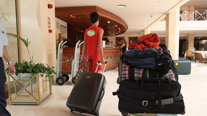 Una familia entra, aompañada de sus maletas, a la recepción de un hotel.