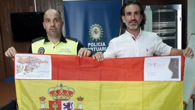 López y Siles posando con una bandera de España con los logos de sus patrocinadores.