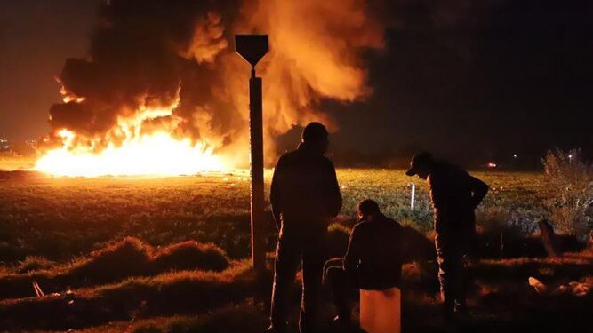 Tres personas observan el fuego sobre un bidón vacío.