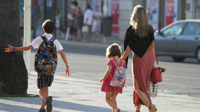 Dos pequeños caminan con su madre de camino al colegio.
