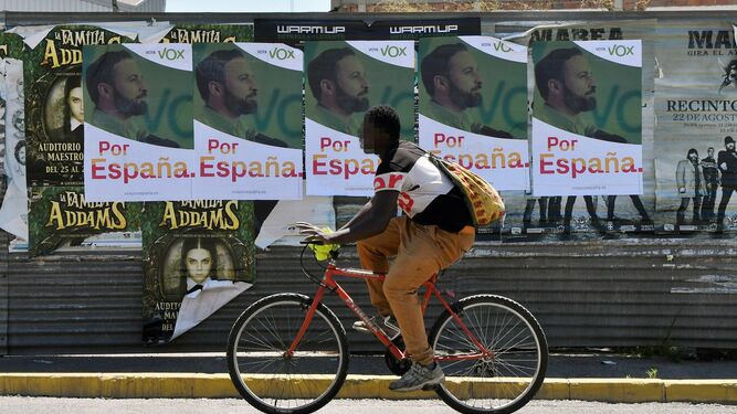 Un inmigrante en bicicleta frente a cartelería de Vox en El Ejido