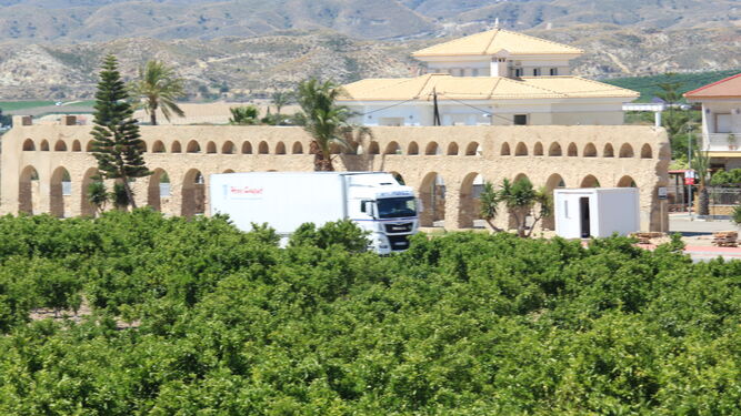 Un camión de una empresa de transporte antense circula junto al acueducto y un campo de naranjos.
