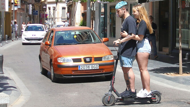 Dos jóvenes cruzan un paso de peatones sobre un patinete eléctrico en Almería capital.