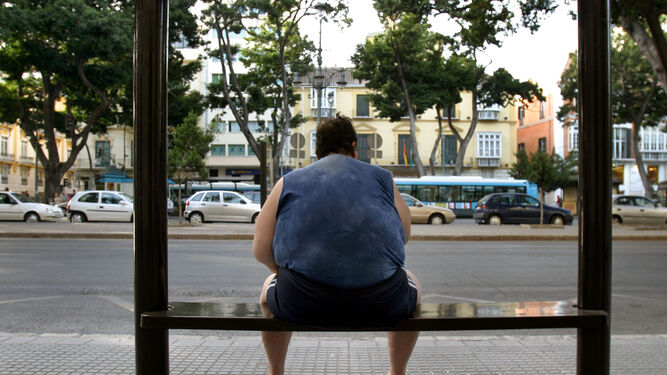 Un hombre obeso sentado en una parada de autobús.