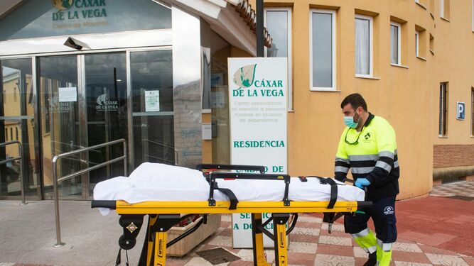 Un sanitario traslada una camilla en una residencia de Cájar (Granada), donde diez ancianos han fallecido.