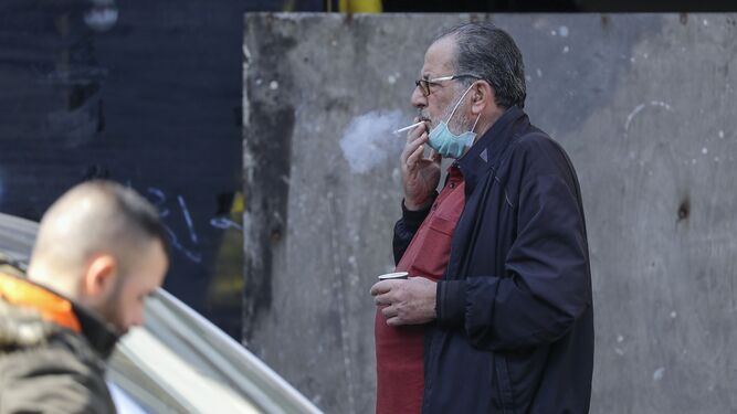 Un hombre fuma un cigarrillo con la mascarilla echada hacia abajo