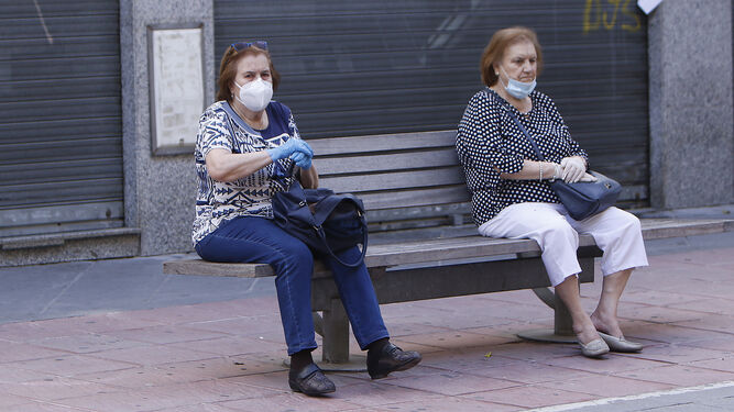 Dos mujeres descansan en un banco público en una calle de Sevilla.