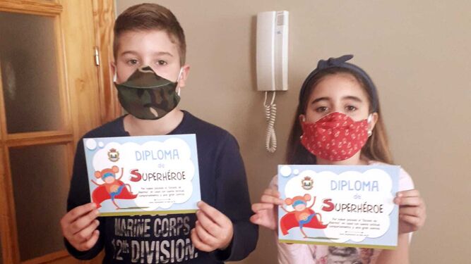 Los pequeños Álvaro y Martina muestran orgullosos sus diplomas de buen comportamiento y las mascarillas con motivos infantiles
