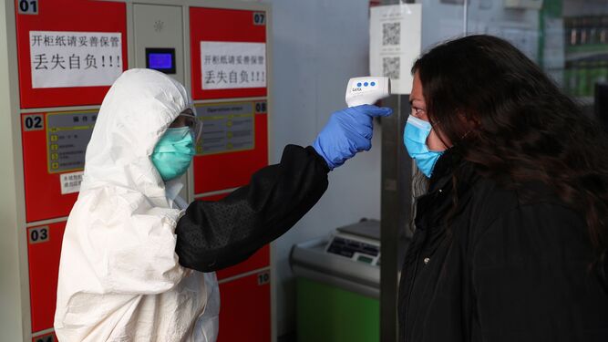 Una trabajadora usa un termómetro  de infrarrojos  para tomar la temperatura a los clientes durante la reapertura del supermercado.