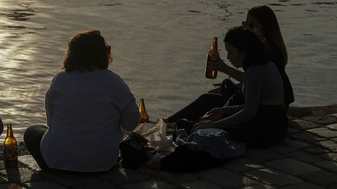 Varios jóvenes consumiendo alcohol junto al río.