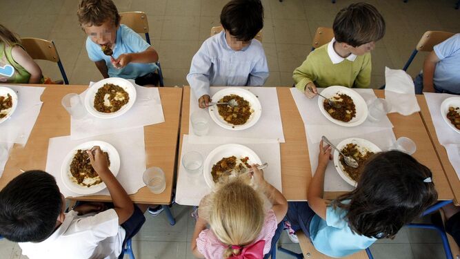 Niños comen un plato de comida en el comedor del colegio.