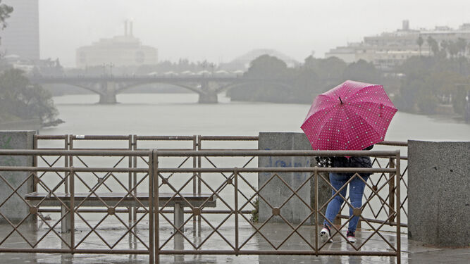 Una mujer pasea con paraguas por el puente de San Telmo.