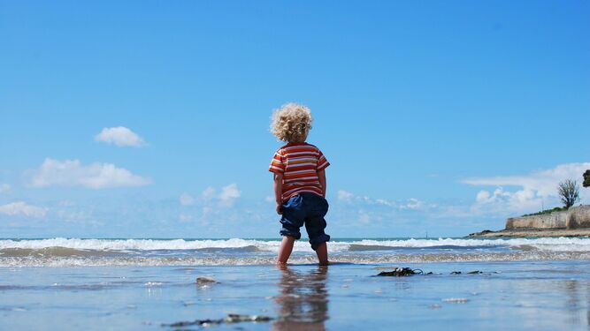 Un niño está en la orilla de la playa mojándose los pies
