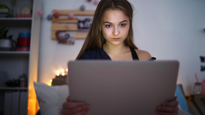 Una joven sentada en su habitación mientras pasa tiempo en su ordenador