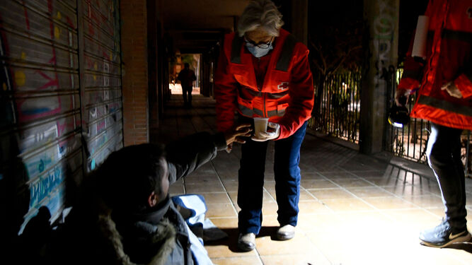 Voluntarios de Cruz Roja entregan una bebida caliente a un indigente.