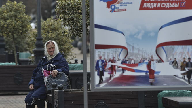 Una anciana descansa junto a un cartel por el noveno aniversario de la anexión de Crimea en Simferopol.