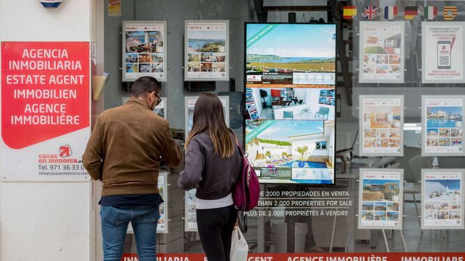 Dos jóvenes observan los carteles de una agencia inmobiliaria