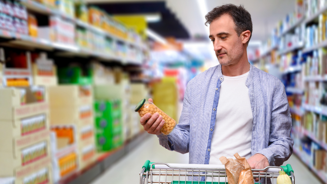 Un hombre consulta la fecha de caducidad de un producto antes de añadirlo a su carrito en el supermercado