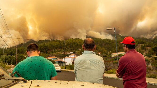 Un grupo de vecinos observa como las llamas queman las montañas.