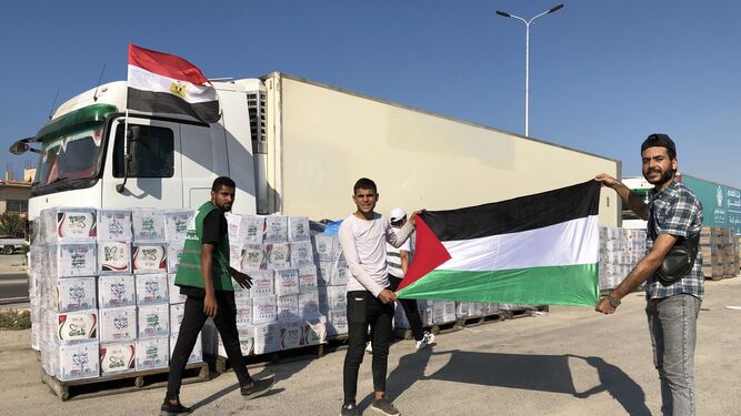 Dos hombres muestran la bandera palestina ante camiones con ayuda humanitaria para Gaza paralizados en Arish, Egipto.