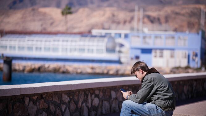 Un joven usa su teléfono móvil sentado en un banco del Paseo Marítimo de la capital almeriense.