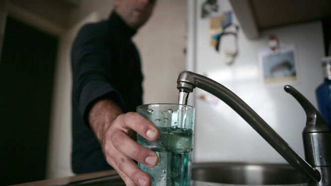 Un hombre sostiene un vaso mientras lo llena de agua del grifo.