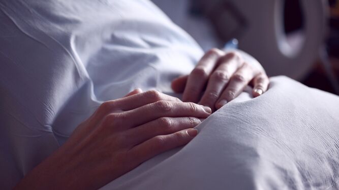 Una mujer, con ropa de hospital, sitúa las manos sobre su abdomen.